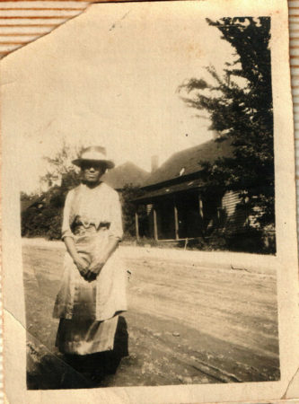 Unknown Black woman in hat in front of house