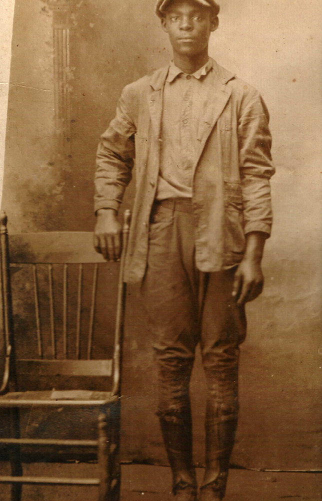 Black man in hat posing by chair