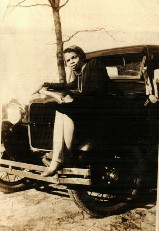 Unknown Black woman sitting on a car