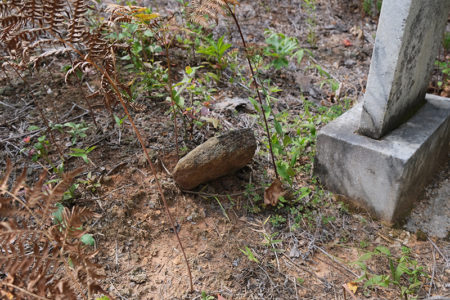 Two graves, one unmarked (center of photo) and one with a headstone (right).